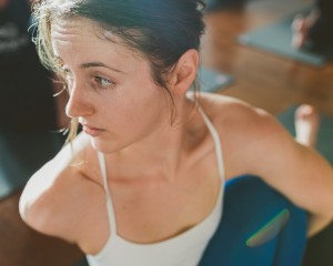 girl wearing white tank top sweating while doing ashtanga yoga asana in mysore style class in the studio at Ashtanga Yoga Victoria